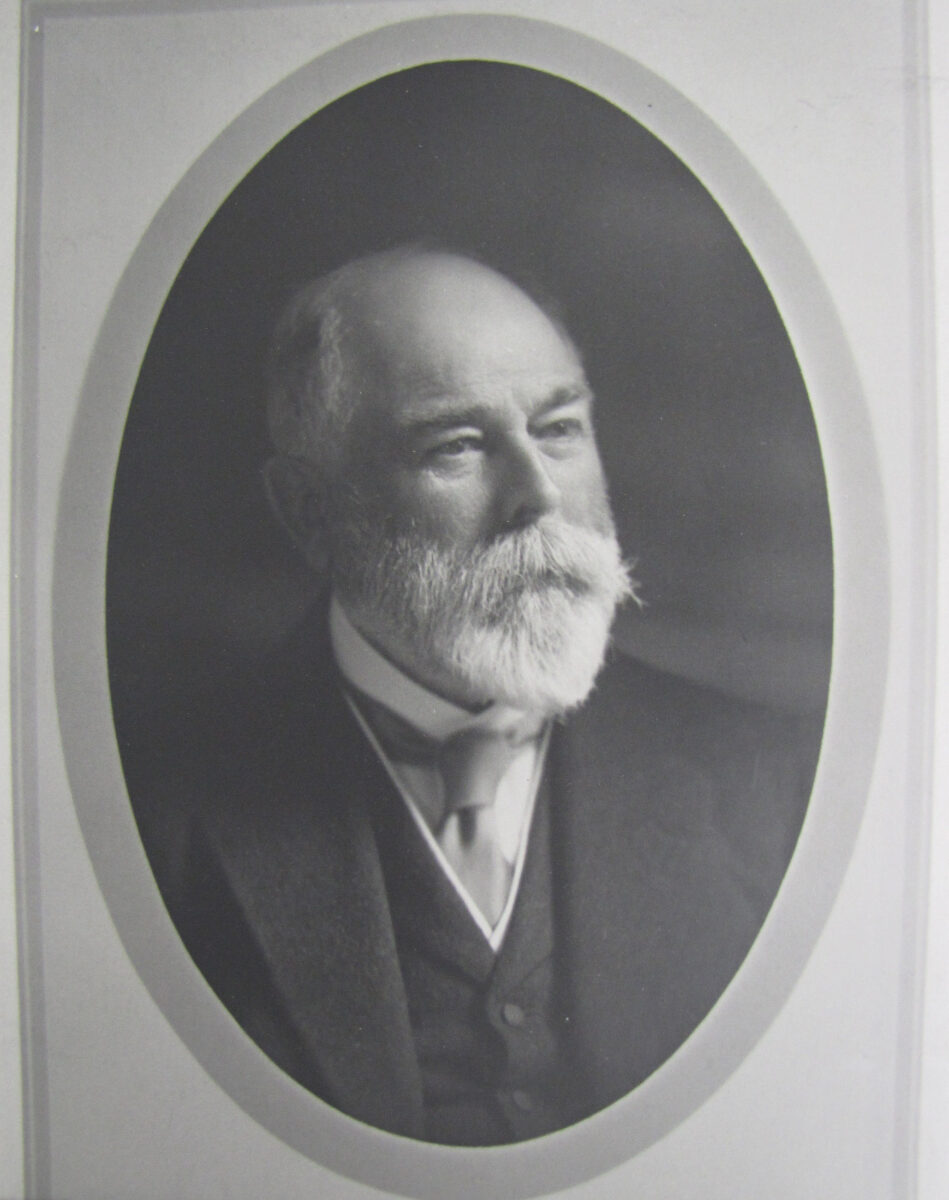 A photograph set in an oval paper matte shows a middle-aged John Labatt Junior staring off to the side of the camera's view. He has a white pointed beard and moustache and is wearing a tie with a dark woolen vest and suit jacket as was common at the time.