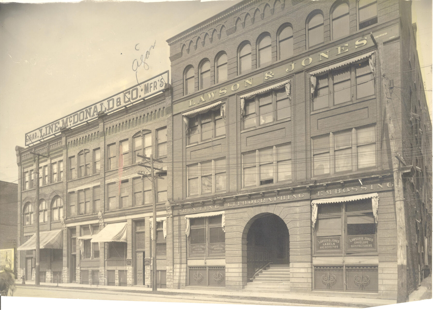 An aged black and white photograph taken from across the street of the Lawson & Jones production facility. The viewpoint shows a 3 story brick building with an arched entrance.