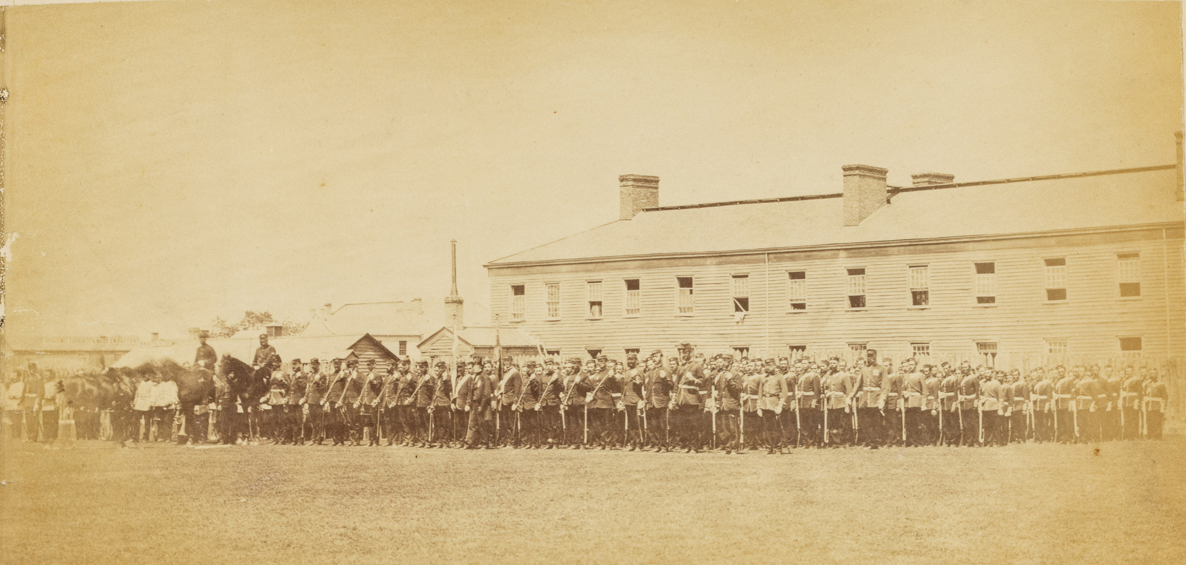 A yellowing old photo of a military company standing outside the Stanley Barracks in London, Ontario